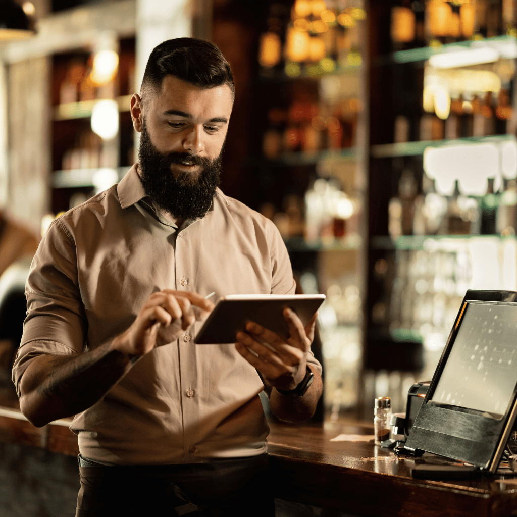 Empleado de restaurante usando una tablet frente a una barra, con un sistema de punto de venta visible, optimizando la gestión con Soft Restaurant